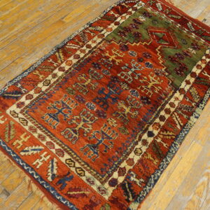 A thick-pile tribal rug featuring rustic red, olive green, and blue geometric patterns on distressed wood floors.