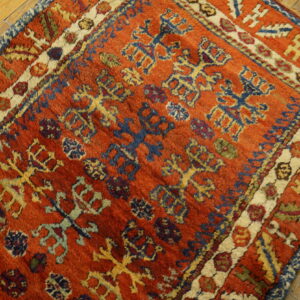 High-pile rug in rust red, blue, and gold geometric patterns rests on distressed wooden floorboards.