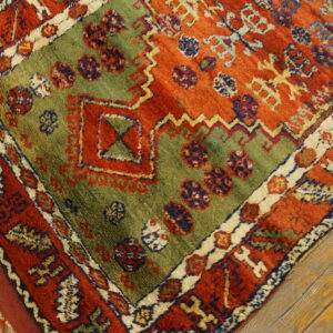 A rust red, olive green, and blue geometric rug with shaggy texture lies on distressed wood flooring.