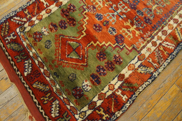 A rust red, olive green, and blue geometric rug with shaggy texture lies on distressed wood flooring.