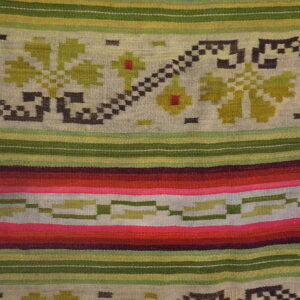 Flatweave rug displays bright red, pink, and green stripes and geometric floral patterns on wood flooring.