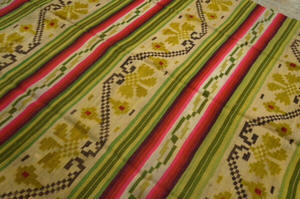 Brightly striped rug in pink, red, and green with beige sections showcasing geometric olive floral patterns.