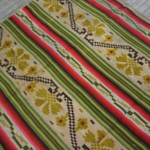 Flatweave rug with colorful diagonal stripes and floral patterns rests on distressed gray wooden floor.