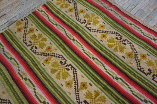 Flatweave rug with colorful diagonal stripes and floral patterns rests on distressed gray wooden floor.