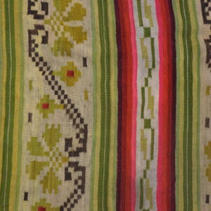 A brightly colored striped flatweave rug with geometric and floral patterns rests on whitewashed plank flooring.