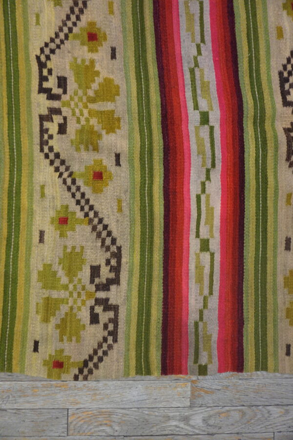 A brightly colored striped flatweave rug with geometric and floral patterns rests on whitewashed plank flooring.