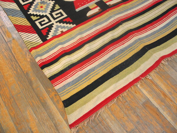 Red, black, and multicolor striped flatweave rug with geometric patterns displayed on rustic hardwood floors.