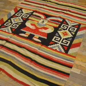Flatweave rug with colorful stripes, geometric patterns, and a central human figure on distressed wood.