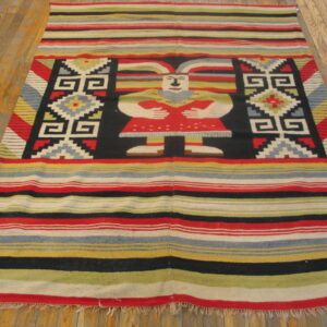 A multi-color striped flatweave rug features a central figural and geometric design resting on hardwood planks.
