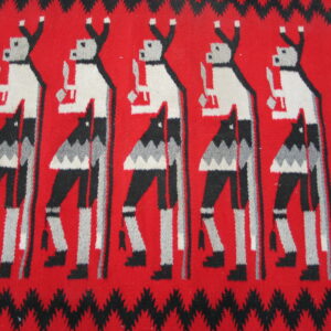 Red woven rug detail with repeating stylized black, white, and gray dancing figures and zigzag borders.
