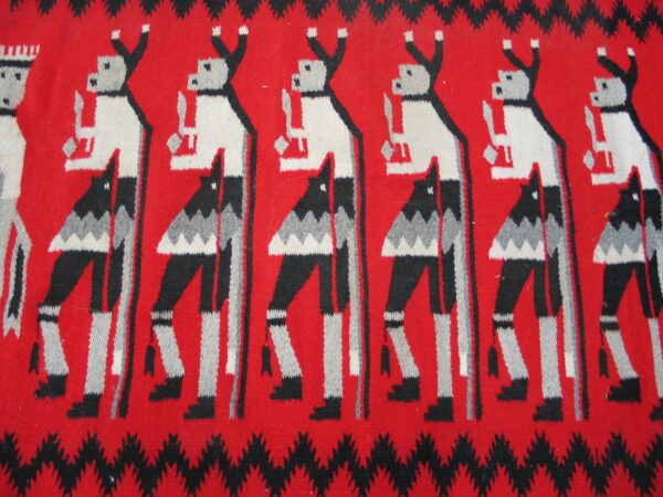 Red woven rug detail with repeating stylized black, white, and gray dancing figures and zigzag borders.