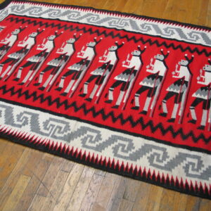 Red, black, gray, and white flatweave rug featuring stylized figures and a meander border on a wood floor.