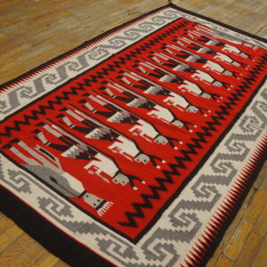 Red flatweave rug with repeating black and white figures and a grey key pattern border on wood planks.