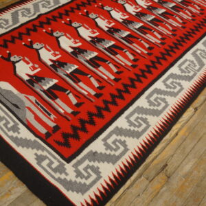 Low-pile red, black, grey, and white rug with repeating figures rests on distressed wood planks.