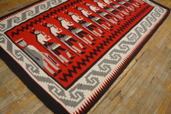 Low-pile red, black, grey, and white rug with repeating figures rests on distressed wood planks.