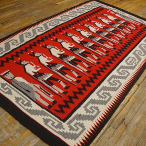Red, gray, and black flatweave rug featuring stylized figures and a geometric border on distressed wood flooring.