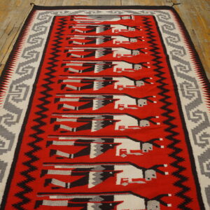 Red runner rug with gray, black, and white stylized figures rests on worn wood flooring.