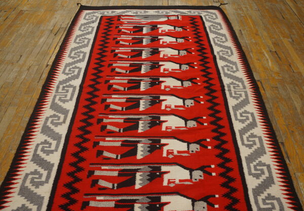 Red runner rug with gray, black, and white stylized figures rests on worn wood flooring.