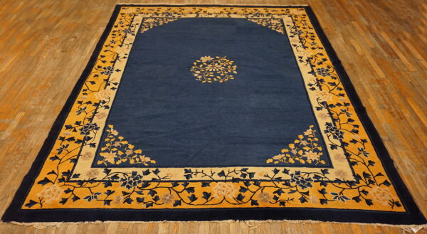 Blue rug with yellow and navy floral borders and a central floral medallion on wood flooring.