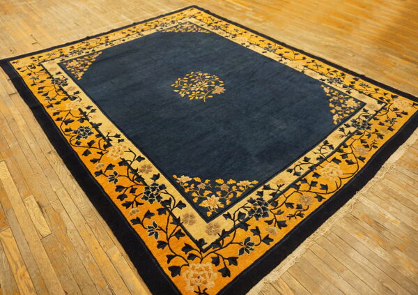 A deep indigo rug with a wide mustard yellow and dark blue floral border rests on worn wood plank flooring.