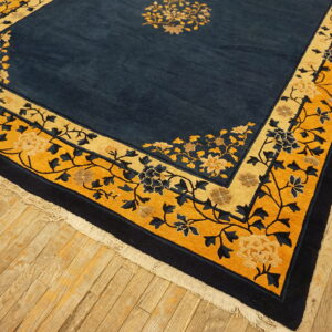 Navy and gold floral rug featuring a medium pile and detailed borders rests on worn plank flooring.