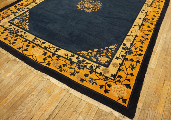 Navy and gold floral rug featuring a medium pile and detailed borders rests on worn plank flooring.
