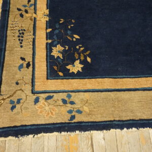 Navy rug with a tan and gold floral border, accented with blue vines, lying on rustic wood floors.