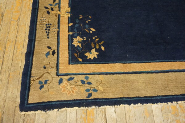 Navy rug with a tan and gold floral border, accented with blue vines, lying on rustic wood floors.