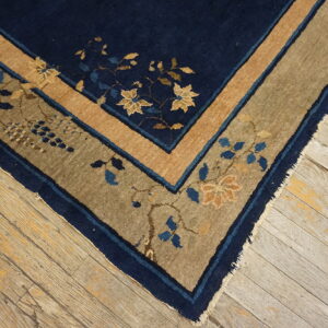 Navy and tan border rug with floral motifs on distressed, light wood flooring.