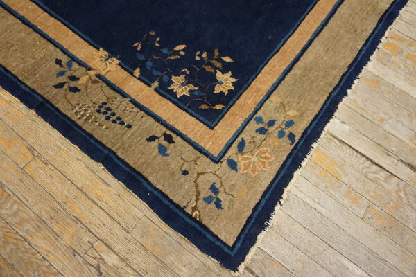 Navy and tan border rug with floral motifs on distressed, light wood flooring.