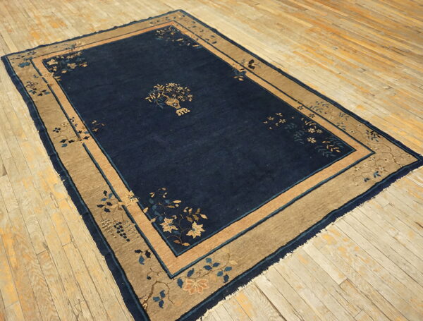 Navy blue rug with tan and light blue floral borders lies on distressed light wood flooring.