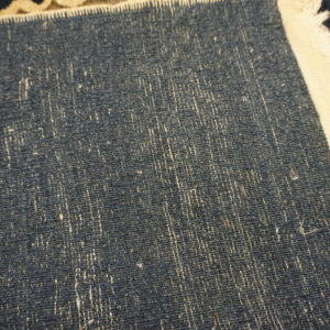 Textured dark blue rug backing detail with vertical white fibers and a broad, frayed cream binding.