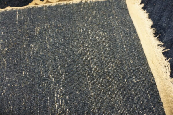 Textured dark blue rug backing detail with vertical white fibers and a broad, frayed cream binding.