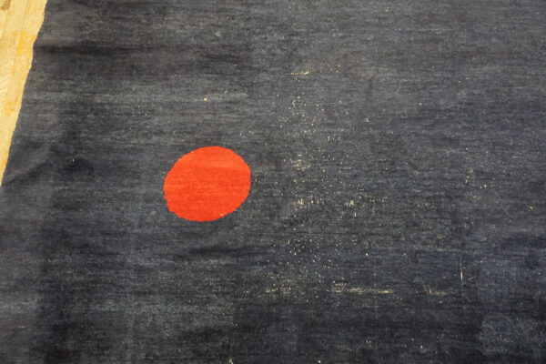 Dark blue textured rug featuring a large, solid red circle rests on light wooden plank flooring.
