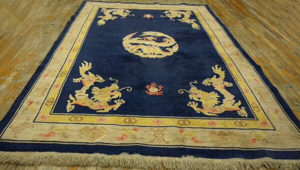 Navy blue rug with yellow dragon motifs and wide cream borders rests on worn wooden planks.