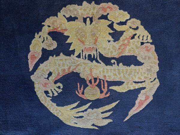 Navy blue rug with a circular, high-pile motif of a yellow and peach dragon.