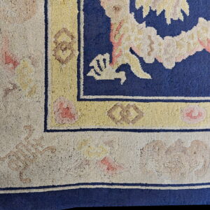 Intricate corner detail of a deep blue rug bordered by textured beige and yellow floral patterns.