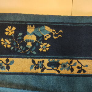 Dark blue rug border detail showing yellow and teal stylized floral and vase patterns.