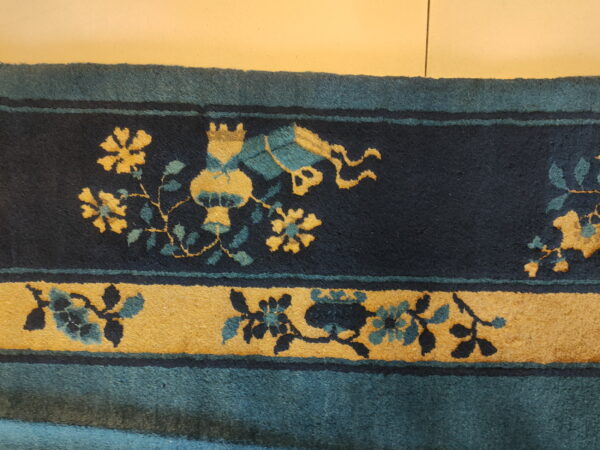 Dark blue rug border detail showing yellow and teal stylized floral and vase patterns.