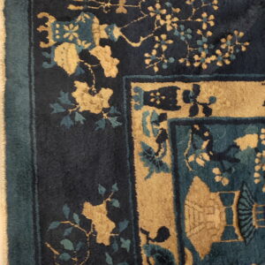 Detail of a plush rug showing dark blue, teal, and gold floral corner design and fringed edge.
