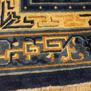 Navy and slate blue rug detail shows gold interlocking geometric borders lying on wood flooring.