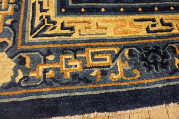 Navy and slate blue rug detail shows gold interlocking geometric borders lying on wood flooring.