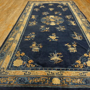Navy blue rug featuring scattered tan and light blue botanicals and a geometric border on wood flooring.
