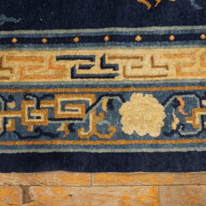 Close-up of a navy blue, tan, and cream bordered rug showing geometric patterns on distressed wood flooring.