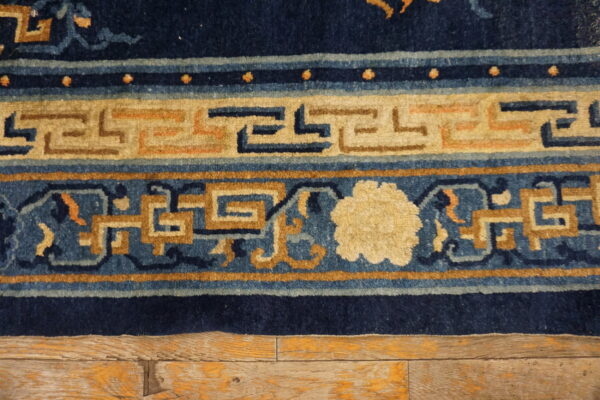Close-up of a navy blue, tan, and cream bordered rug showing geometric patterns on distressed wood flooring.