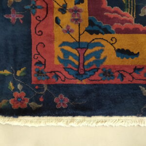Navy rug with a multicolored floral and geometric design, yellow center field, red accents, and visible white fringe.