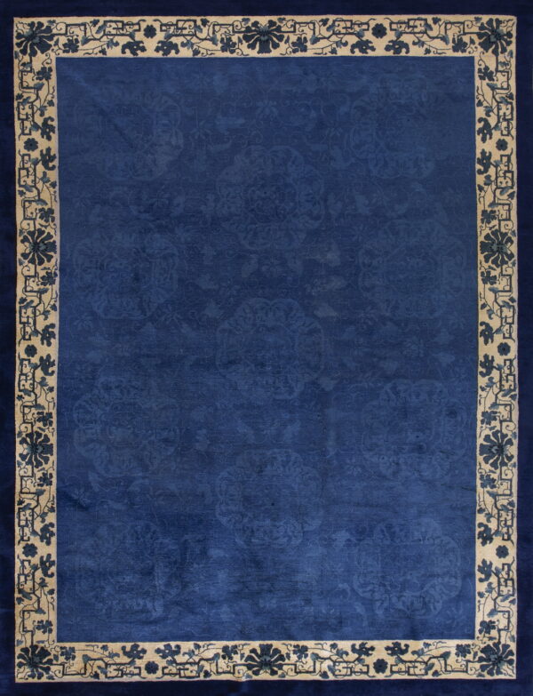 Rectangular deep blue rug featuring a tone-on-tone field and a wide beige border with blue floral designs.