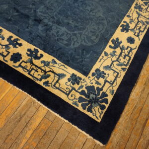 Dark blue rug featuring a tan and floral border detail rests on rustic wooden planks.