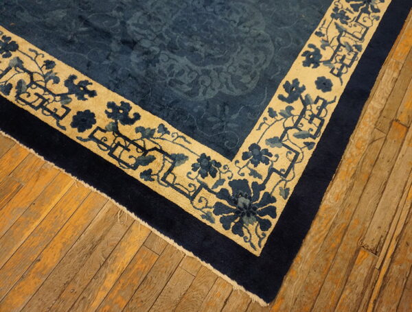 Dark blue rug featuring a tan and floral border detail rests on rustic wooden planks.