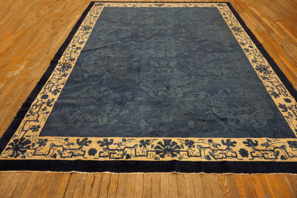 A navy blue rug with subtle floral patterns and a wide beige floral border rests on warm hardwood flooring.